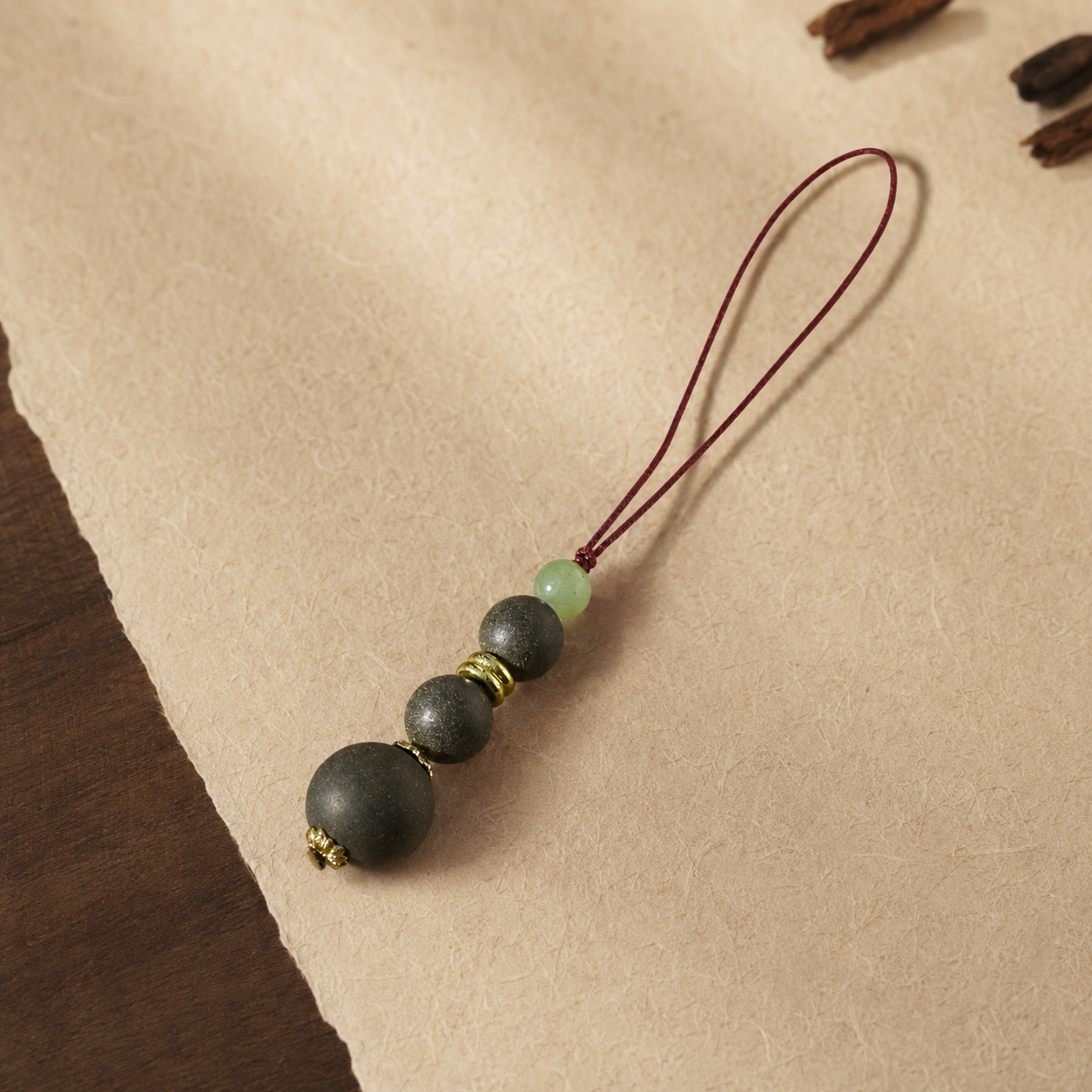 Burgundy cord phone charm with three dark He Xiang beads, a pale green glass bead and gold-toned spacers