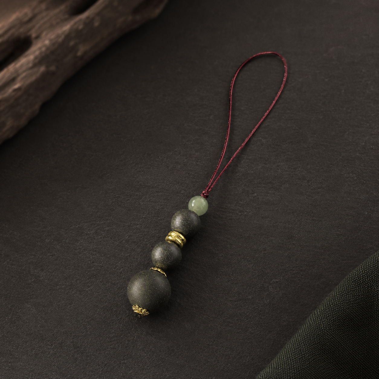 Burgundy cord phone charm with three dark He Xiang beads, a pale green glass bead and gold-toned spacers
