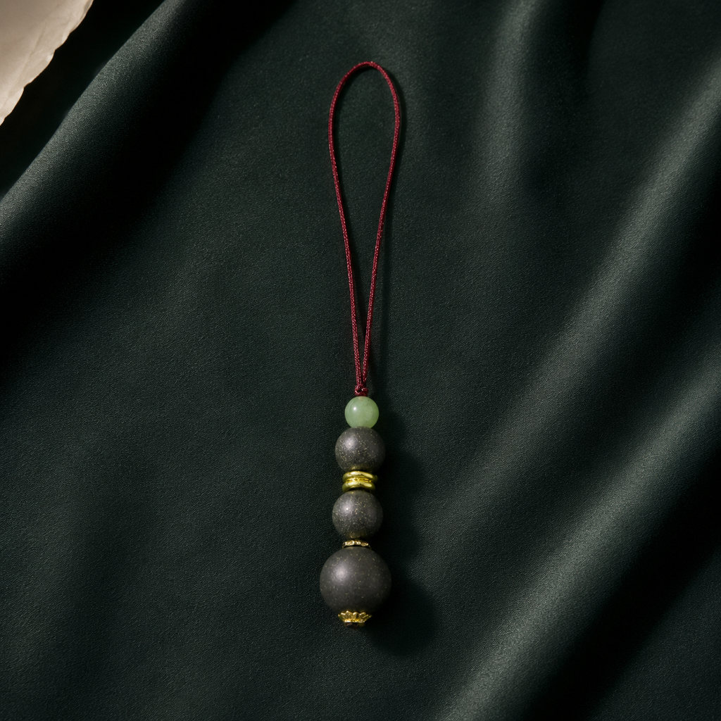 Burgundy cord phone charm with three dark He Xiang beads, a pale green glass bead and gold-toned spacers